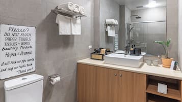 Un bagno moderno con un WC, lavandino e doccia. Un cartello è appeso al muro e c'è un portascopevoli con asciugamani.