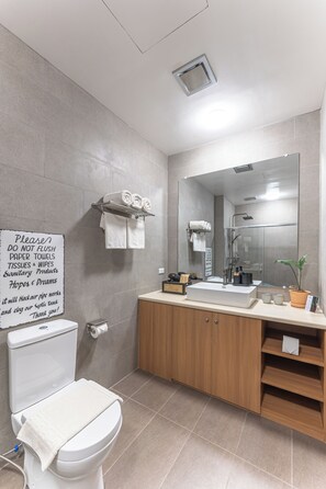 Un baño moderno con inodoro, lavamanos y ducha. Hay un letrero en la pared y un perchero con toallas.