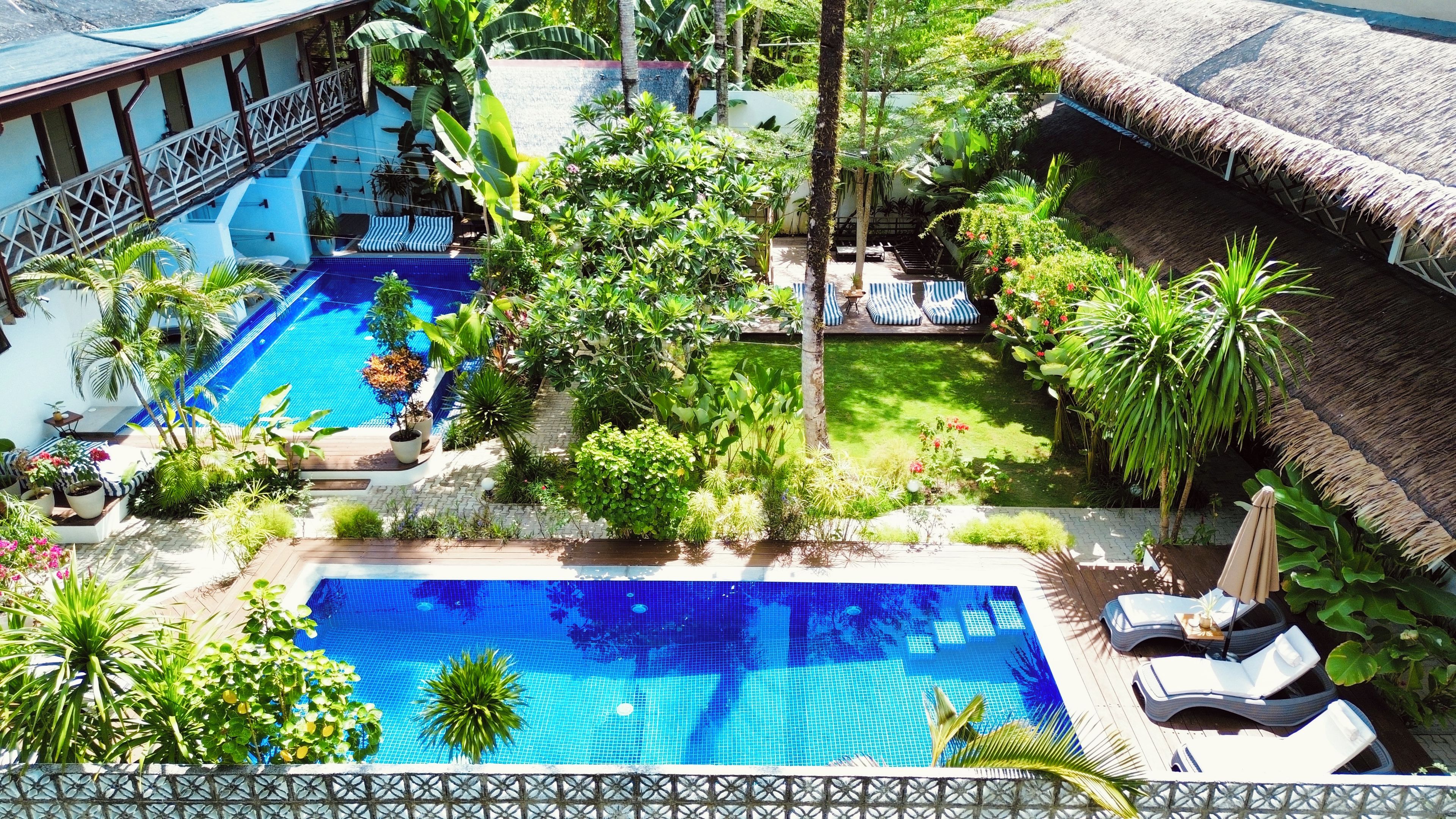 A pool area with a thatched roof, lounge chairs, and various plants.