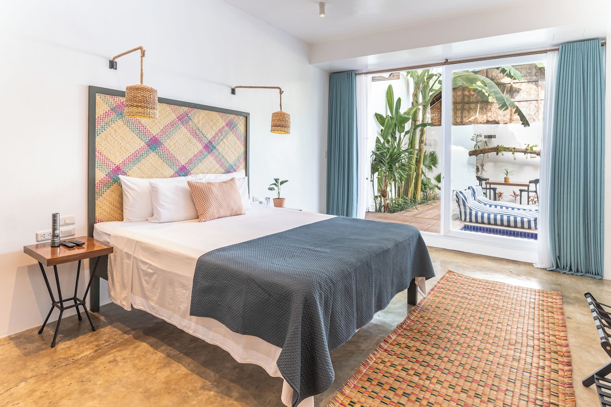 Quarto com cama, mesa de cabeceira e vista para a área externa.