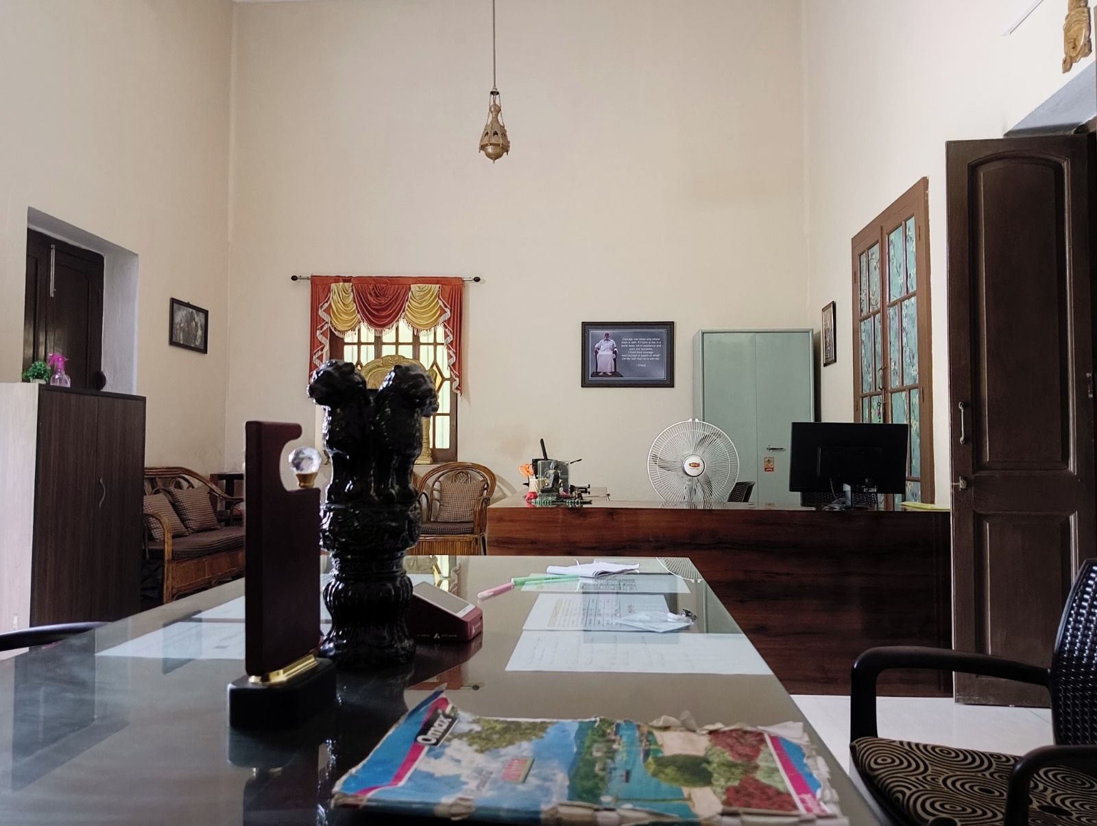 A room with a glass table, a decorative sculpture, a fan, a television, and a cabinet.