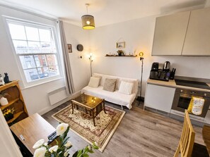 A modern living room with a sofa, coffee table, and a view of the city through a large window. - Contemporary Cabot Circus Central Flat | Sleeps 4 (Saint Paul's)