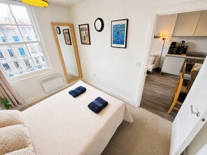 A bedroom with a bed, a bedside table, a mirror, and a view of a cityscape through a window. - Contemporary Cabot Circus Central Flat | Sleeps 4 (Saint Paul's)