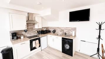 Een moderne keuken met witte kastjes, een vaatwasser, een wasmachine en een flatscreen televisie aan de wand.