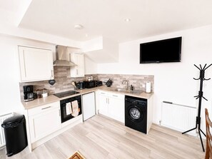 A modern kitchen with white cabinets, a dishwasher, a washing machine, and a flat-screen TV mounted on the wall.
