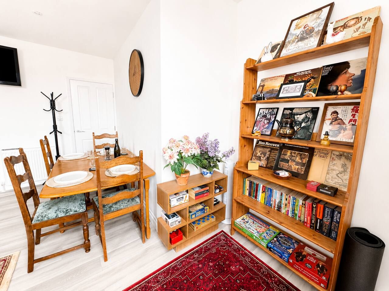 Een eethoek met een houten tafel en stoelen, een boekenplank vol boeken en ingelijste foto's, en een kleine plant op een bijzettafeltje.