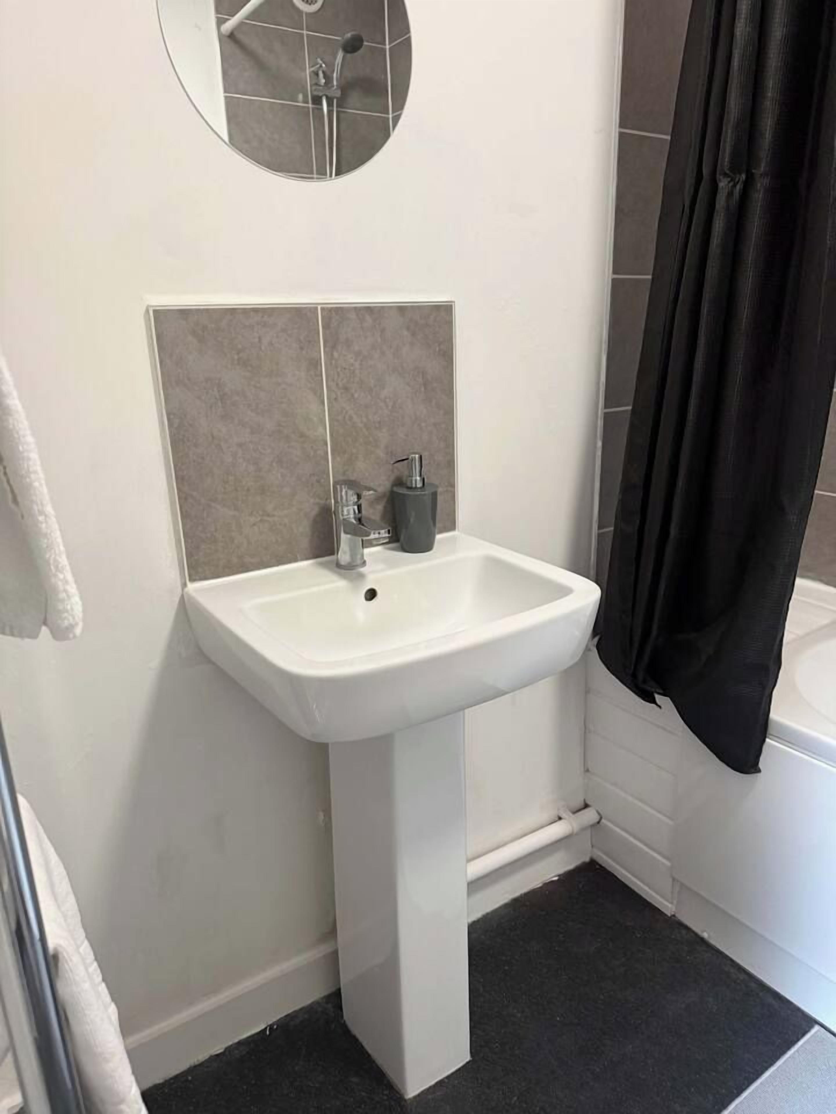 Een badkamer met een witte wastafel op een voetstuk, een spiegel erboven en een zwart douchegordijn.