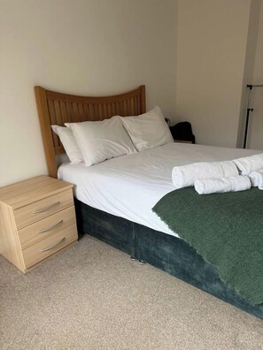 Un lit bien fait, avec du linge de lit blanc, une tête de lit en bois et un plaid vert.