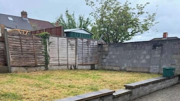 Ein gepflasterter Weg, an einer Seite eine niedrige Steinmauer und an der anderen ein Holzzaun.