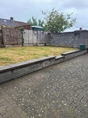 Un chemin pavé, bordé d’un côté par un petit muret en pierre et de l’autre par une clôture en bois.