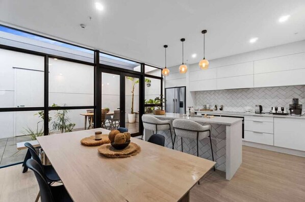 A modern kitchen with white cabinets, a wooden dining table, and pendant lighting.