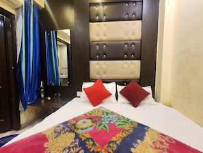 A hotel room with a bed, a mirror, a bathroom visible through the door, and a colorful rug. - Oly Hotel Heritage Inn (New Delhi)