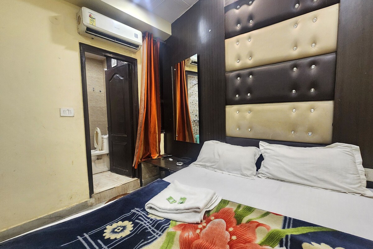 A hotel room with a bed, a bathroom with a mirror, and an air conditioning unit.