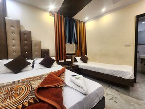 A hotel room with two beds, a large window with curtains, a bedside table, and a bathroom visible through an open door. - Oly Hotel Heritage Inn (New Delhi)