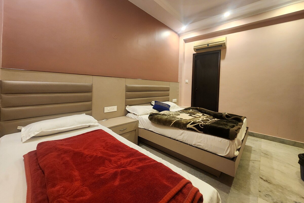 A hotel room with two beds, a red blanket on one bed, and a black door.