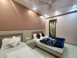 A hotel room with a bed, bedside tables, a nightstand, a mirror, and a ceiling fan. - Oly Hotel Heritage Inn (New Delhi)