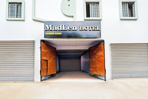 Ein Hotel Eingang mit einem Schild, auf dem 'MadLen Hotel Premium Rooms' steht, und zwei geschlossene Garagentore an jeder Seite.