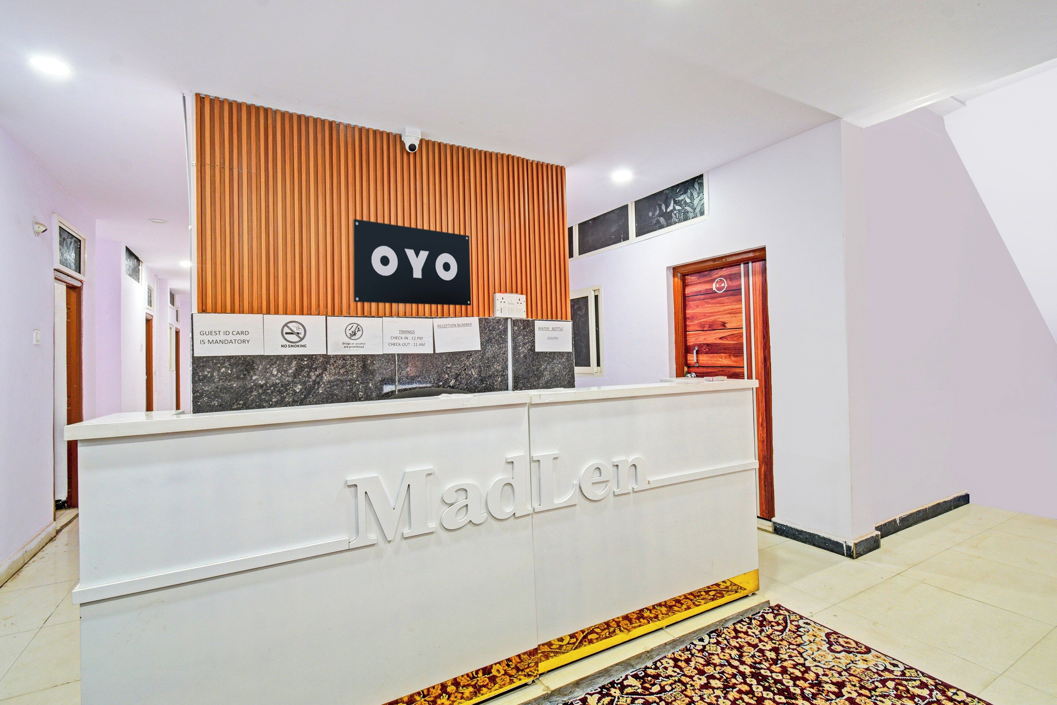 A reception desk with 'Madlen' branding, a 'NO SMOKING' sign, and a 'GUEST ID CARD IS MANDATORY' notice.