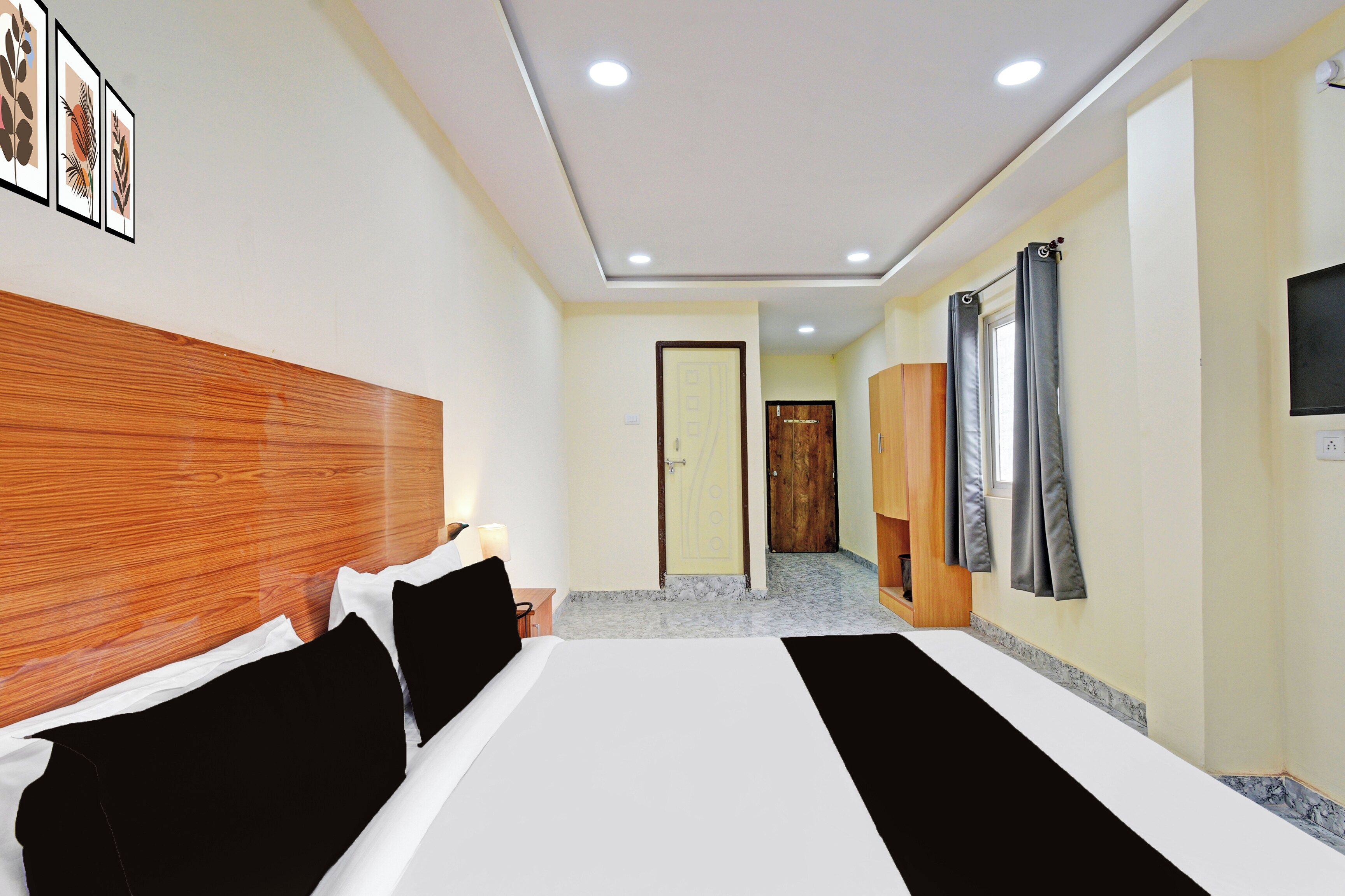 A hotel room with a large bed, a wooden headboard, a flat-screen TV, and a bathroom with a wooden door.