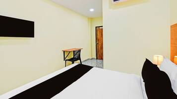 A hotel room with a bed, a desk, an air conditioner, and a door leading to another room.