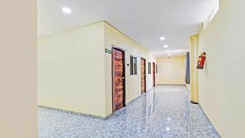 A hallway with marble flooring, wooden doors, and a fire extinguisher mounted on the wall.