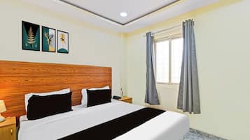A hotel room with a bed, a nightstand, a lamp, a window with curtains, and two wall art pieces.