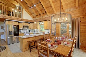 A spacious kitchen with wooden cabinetry, a central island, and a dining area with a wooden table set for four. - Mtn Views from Every Deck without The Mtn Drive! (Maggie Valley)