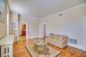 A living room with a glass coffee table, a patterned sofa, wooden flooring, and a white door leading to another room. - Wilmette Condo: 3 Mi Downtown Evanston (Wilmette)