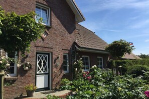 A brick house with a white door, windows, and a garden with various plants and flowers. - Holiday home in Oevenum with swimming pool (Oevenum)