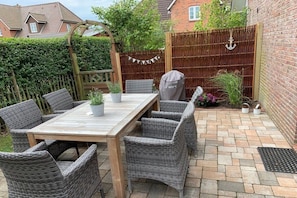 An outdoor patio with a wooden table and wicker chairs, a barbecue grill, and a wooden fence. - Holiday home in Oevenum with swimming pool (Oevenum)