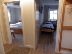A narrow hallway leading to a bedroom with a bed, a bedside table, and a window. - Holiday Apartment With 2 Bedrooms (Zingst)