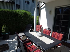 An outdoor patio with a table and chairs, surrounded by a hedge and a building. - Holiday Apartment With 2 Bedrooms (Zingst)