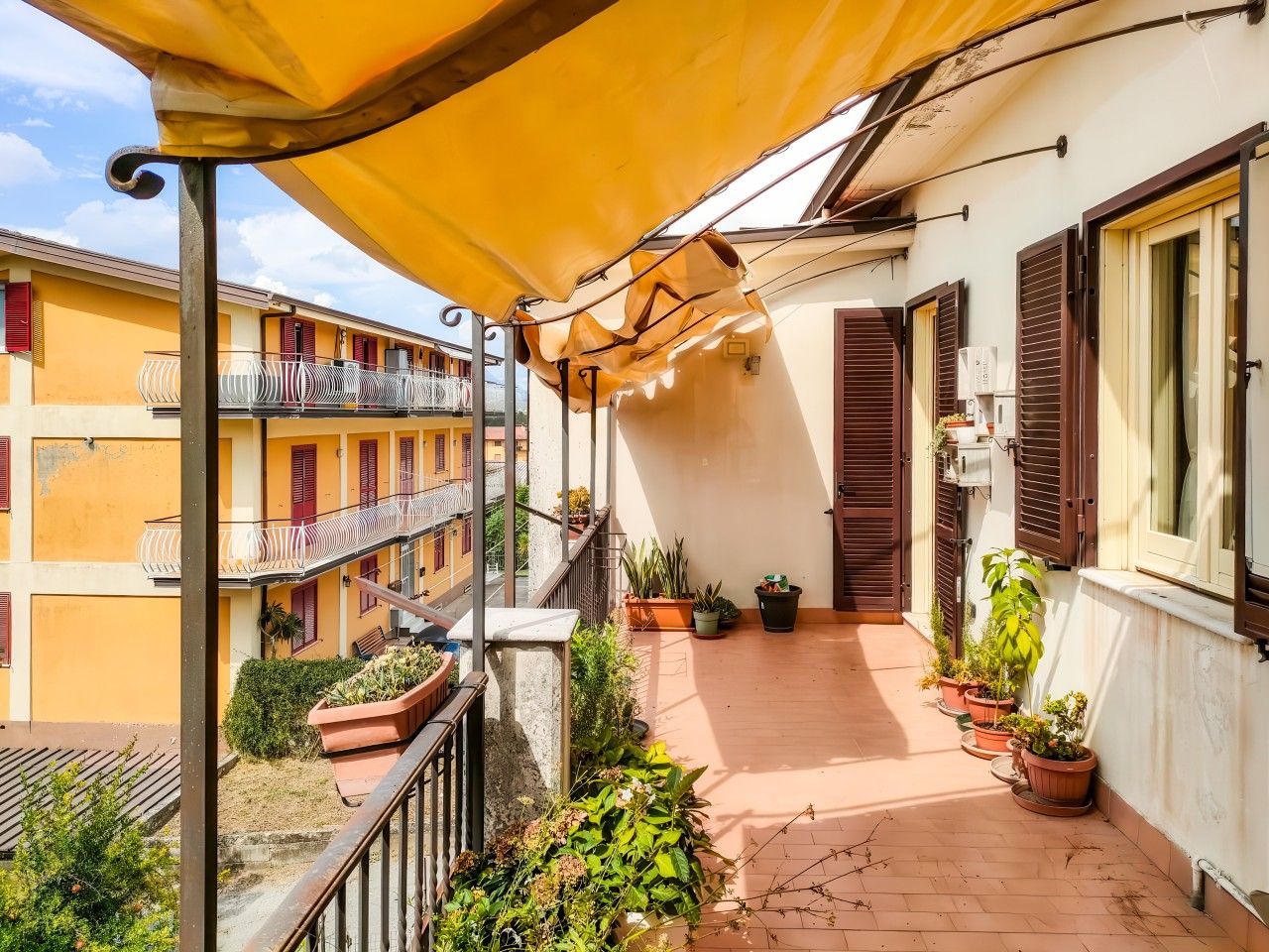 Un balcon agrémenté de plantes en pot, une marquise jaune et une vue sur les bâtiments voisins.