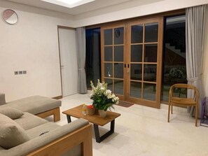 Un soggiorno moderno con un divano, un tavolino da caffè e una poltrona. Una porta scorrevole in vetro dà accesso a un'area esterna.