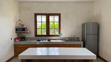 A kitchen with a central island, wooden cabinets, a stainless steel refrigerator, and a window with a view of greenery.