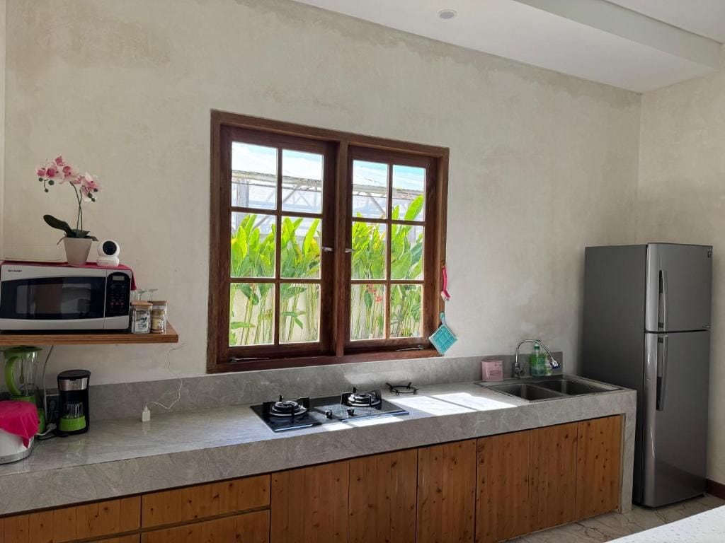 A kitchen with a window, a microwave, a refrigerator, and a sink.