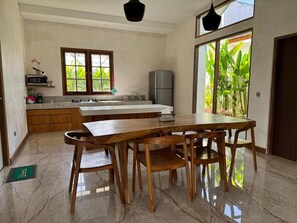 Una cucina con un tavolo e sedie di legno, un frigorifero e una finestra vista verde.