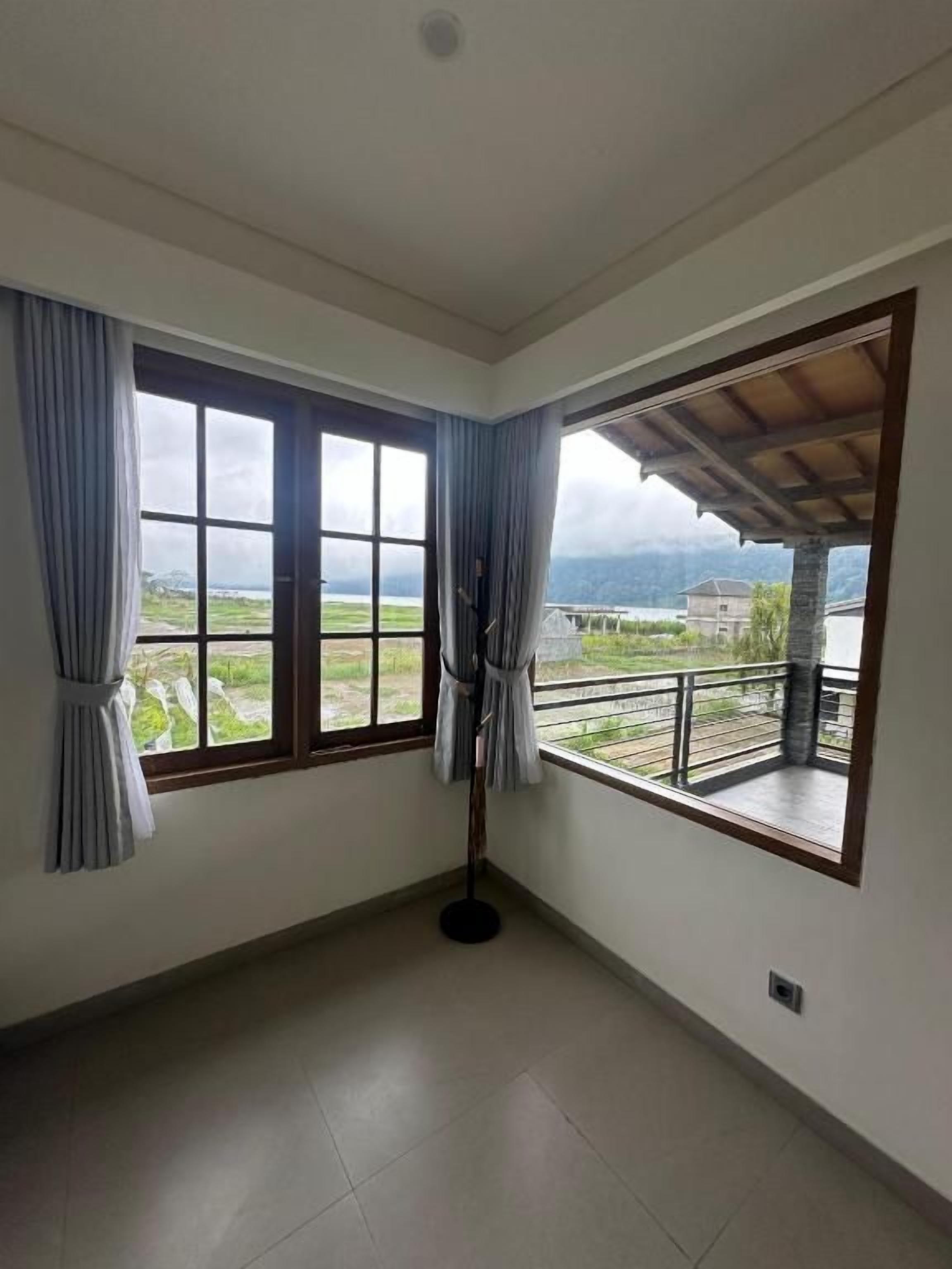 A room with two large windows, a balcony, and a view of a landscape.