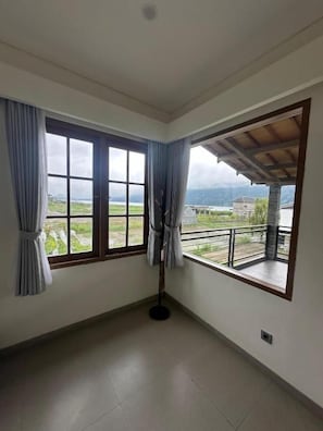 A room with two large windows, a balcony, and a view of a landscape.