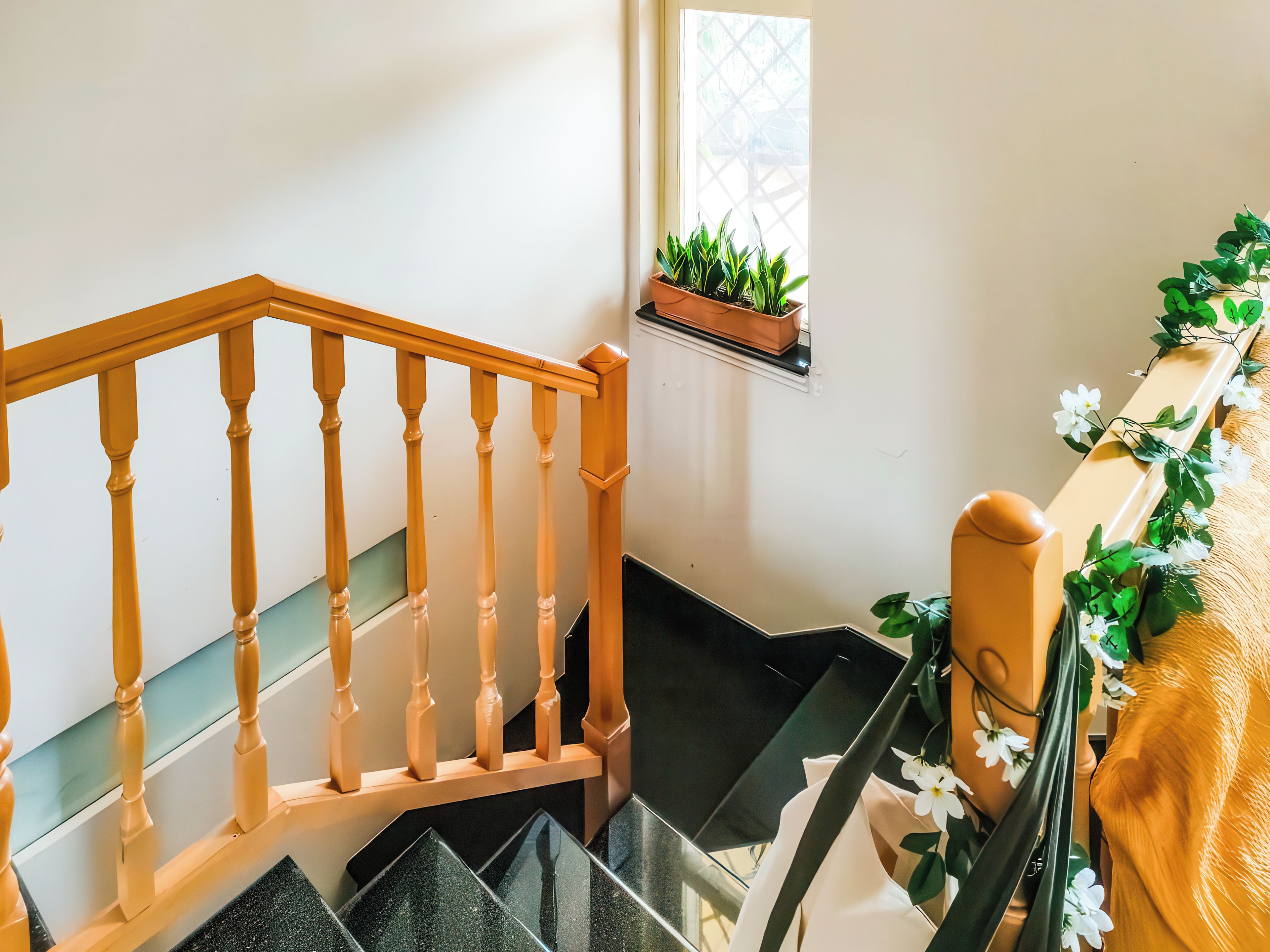 Un escalier avec des balustrades en bois, une petite fenêtre ornée de plantes et une étagère murale décorée de fleurs.
