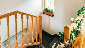 Un escalier avec des balustrades en bois, une petite fenêtre ornée de plantes et une étagère murale décorée de fleurs.