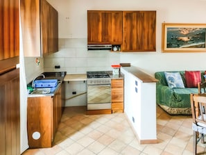 Een kleine keuken met houten kastjes, een fornuis en een spoelbak.