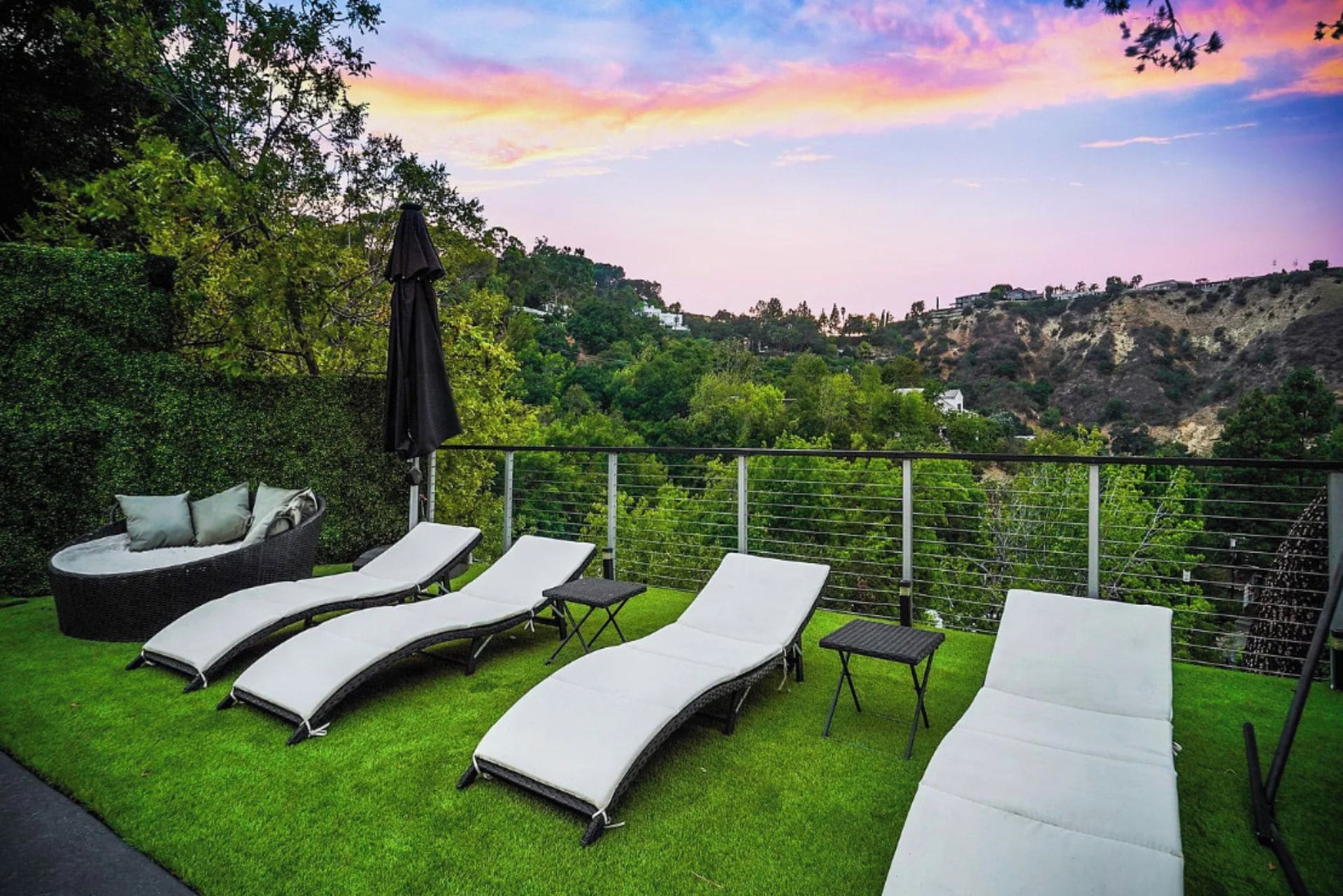 A rooftop terrace with lounge chairs and a table, overlooking a hilly landscape.