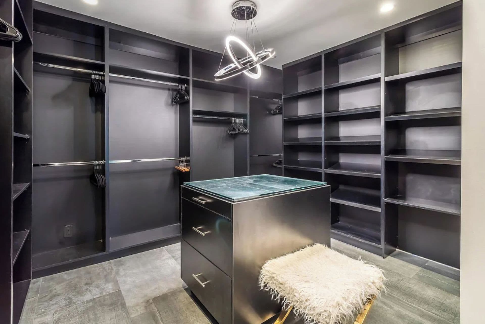 A modern closet with built-in shelves and drawers, a marble countertop, and a fluffy white bench.
