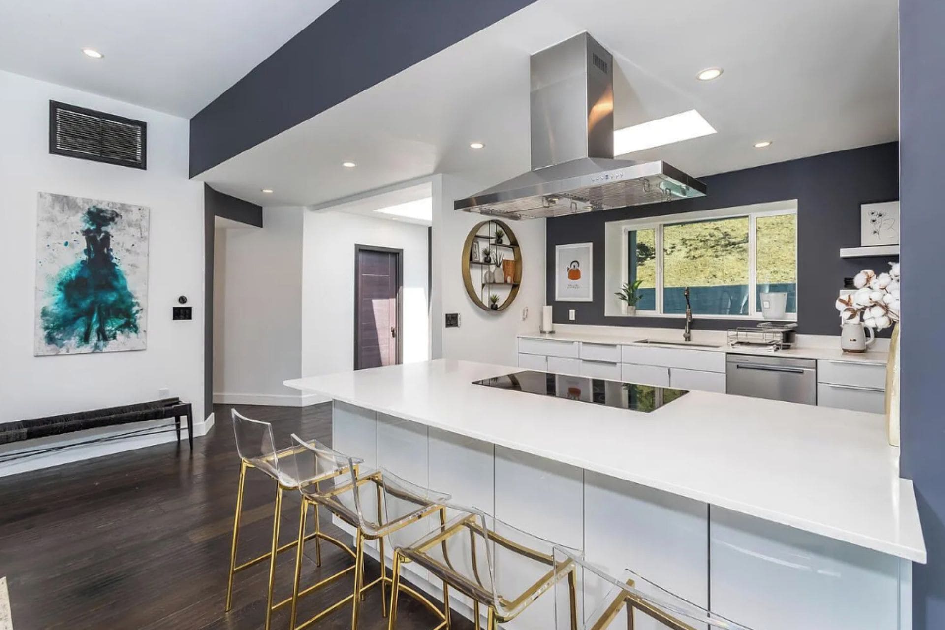 A modern kitchen with a central island, bar stools, and a large window.