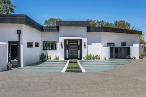 A modern two-story house with a flat roof, a front entrance with a black door, and a small garden area with a pathway leading to the entrance. - Oakfield Rise (Sherman Oaks)