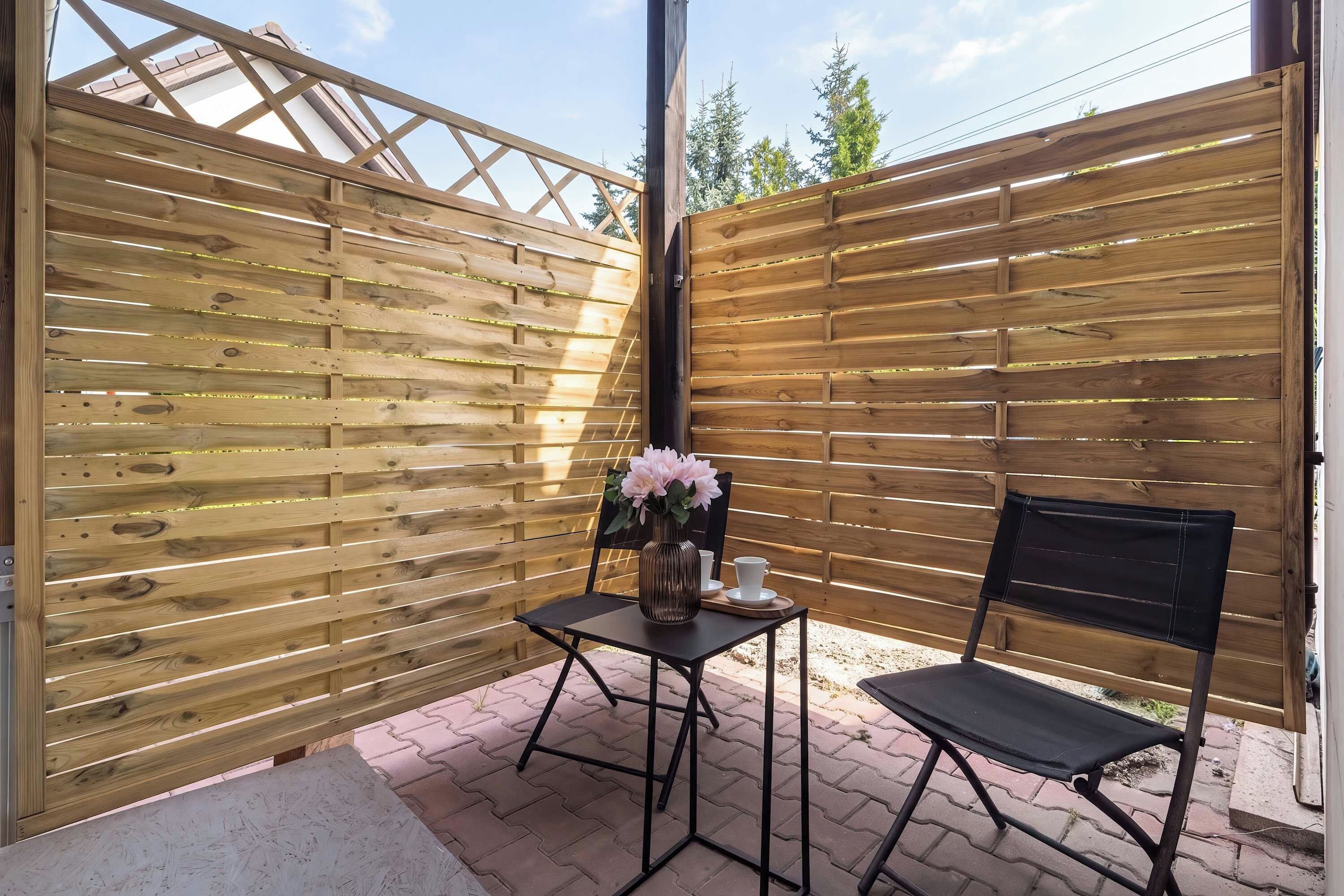 A private outdoor terrace enclosed by a wooden privacy fence, furnished with a small table and two chairs.