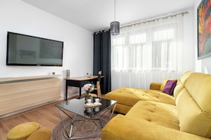 A modern living room with a yellow sofa, a glass coffee table, a flat-screen TV, and a dining area with a wooden desk and chair. - Spacious House in a Quiet Neighbourhood of Poznan by Noclegi Renters (Poznań)
