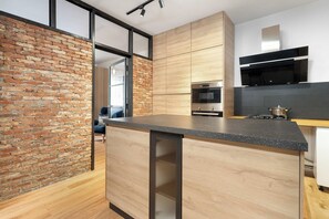 Una cocina moderna con pared de ladrillo, armarios de madera, horno de acero inoxidable y encimera negra.