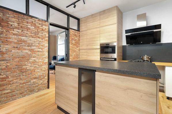 Une cuisine moderne avec un mur en briques, des armoires en bois, un four en acier inoxydable et un plan de travail noir.
